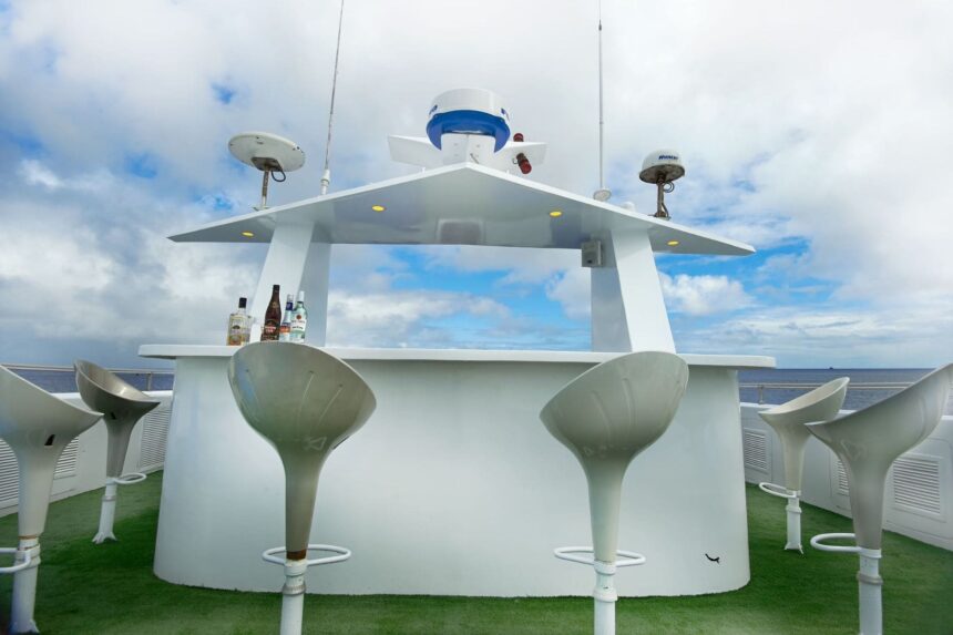 Outdoor bar on the top deck with white stools and bottles set out under a clear sky