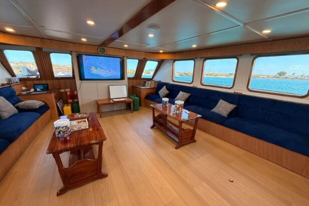 Onboard saloon with blue sofas and a wall-mounted screen showing a dive site map