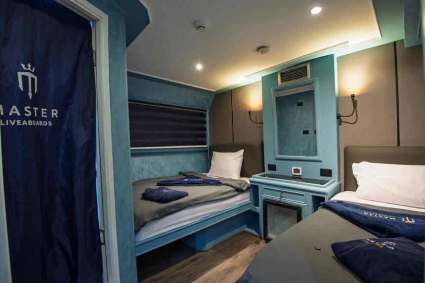 Blue-toned twin cabin with a Master Liveaboards curtain and mirrored beds
