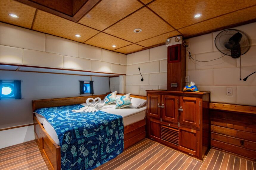 Wood-paneled cabin with a blue patterned bedspread, wall fan and built-in cabinetry