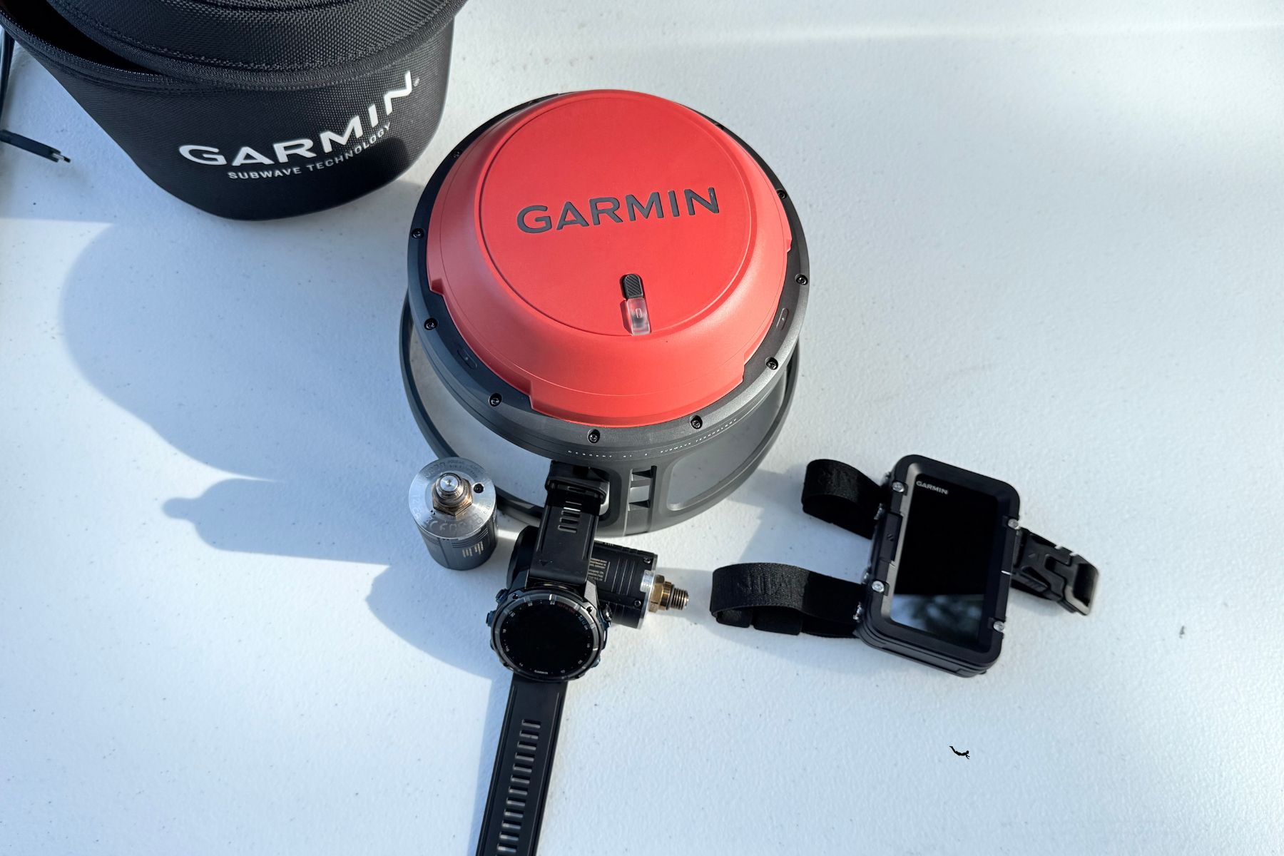 The Garmin Descent S1 Buoy unit, dive watch and mounting hardware laid out on a white surface