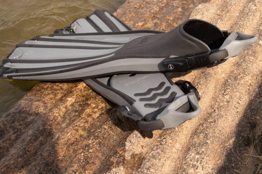 Fourth Element Rec fins in gray resting on a sunlit rock at the water's edge