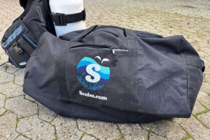 Scuba.com Big Duffel Bag on paving stones with a Cressi BCD and tank standing behind it