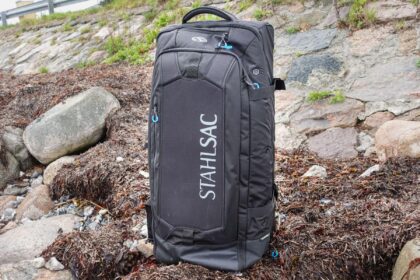 Stahlsac Steel 34 inch rolling bag standing upright on seaweed-covered rocks at the shoreline