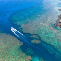 Boat carving a wake through a shallow coral reef near an island resort