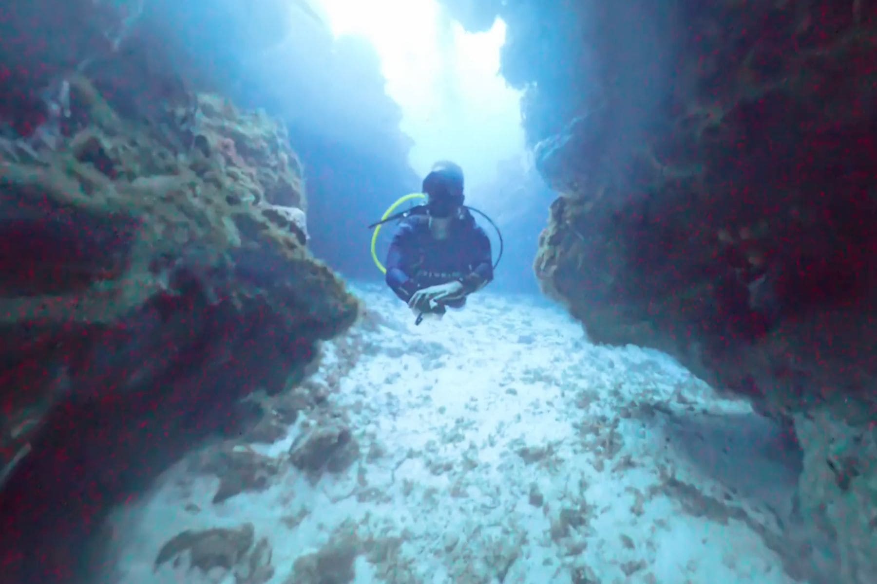 Diver swimming through a narrow coral canyon with light streaming down at Cozumel's Cathedral dive site