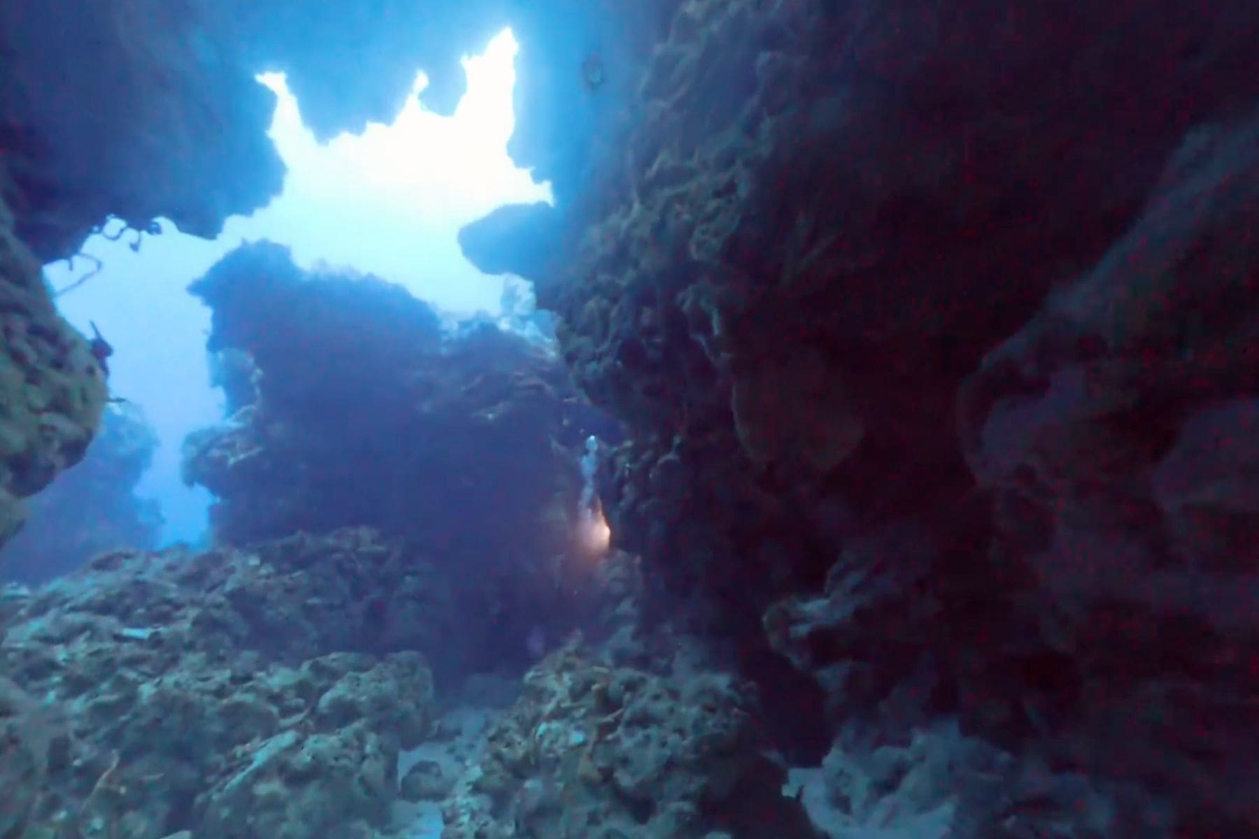 A diver's light glows deep inside a shadowy limestone cavern at Cozumel's Cathedral site