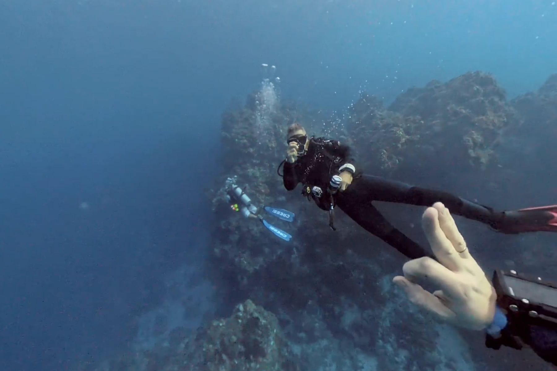 Diver flashing an ok signal while a buddy trails bubbles along a Cozumel reef wall