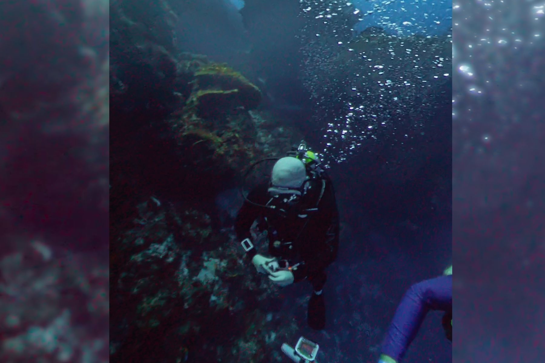 Diver descending along a coral reef wall in Cozumel, bubbles trailing up from the regulator