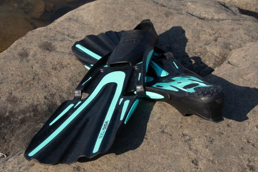 Mares Volo Race fins resting on a sunlit rock, showing the black blades with turquoise accents