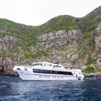 liveaboard dive boat Tiburon Explorer anchored near steep green cliffs in the Galapagos