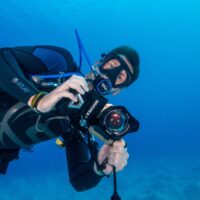 Diver holding an underwater camera rig with a dome port and mounting bracket near the lens