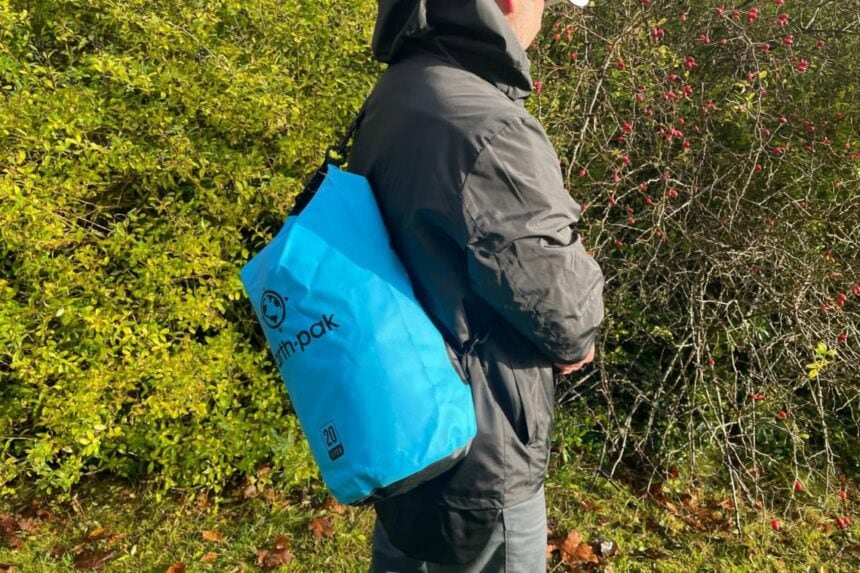 Our tester carrying the blue Earth Pak 20L waterproof dry bag over one shoulder on a hedge-lined trail