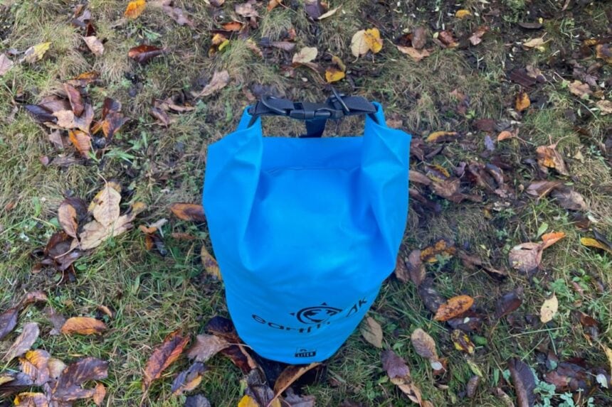 Top-down view of the blue Earth Pak dry bag rolled and buckled, lying on leaf-covered grass