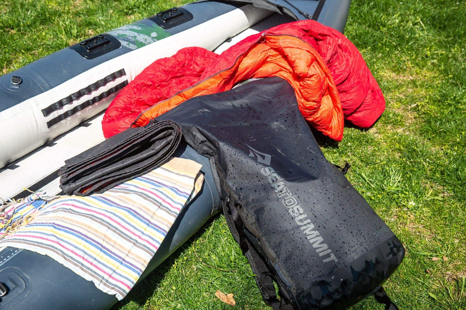 Sea to Summit Big River Dry backpack on grass beside an inflatable boat, sleeping bag and towel