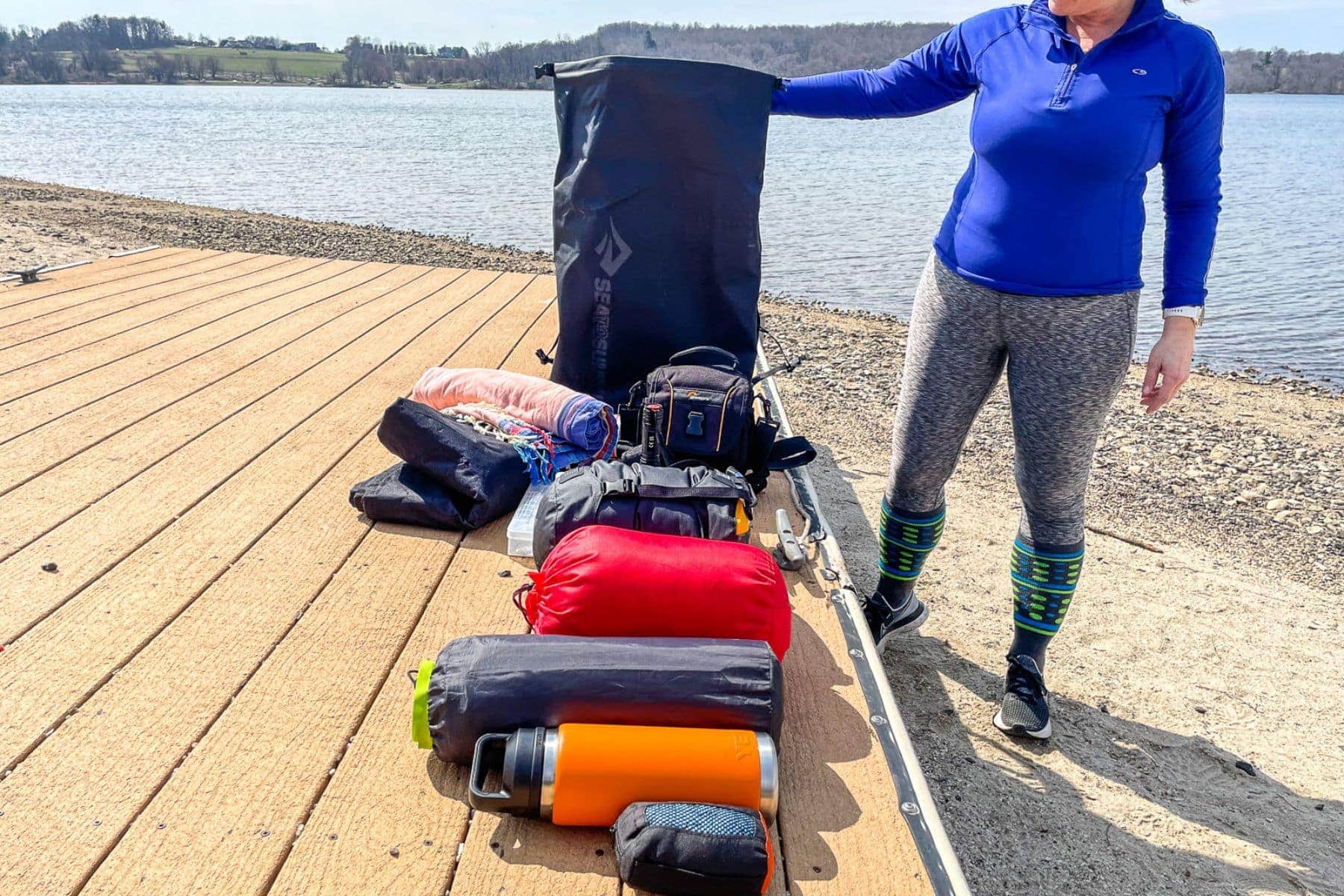 DIVEIN tester on a lake dock with the Sea to Summit Big River dry pack upright beside a spread of camp gear