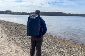 DIVEIN reviewer standing on a pebble lakeshore with the Sea to Summit Big River dry pack on his back