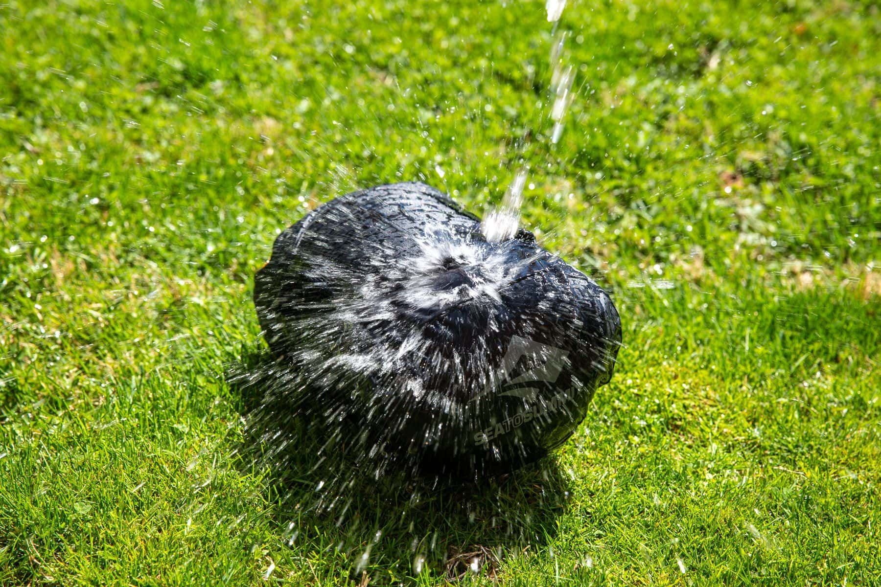 Stream of water poured over the Sea to Summit EVAC Compression HD dry bag on grass, spraying off the fabric