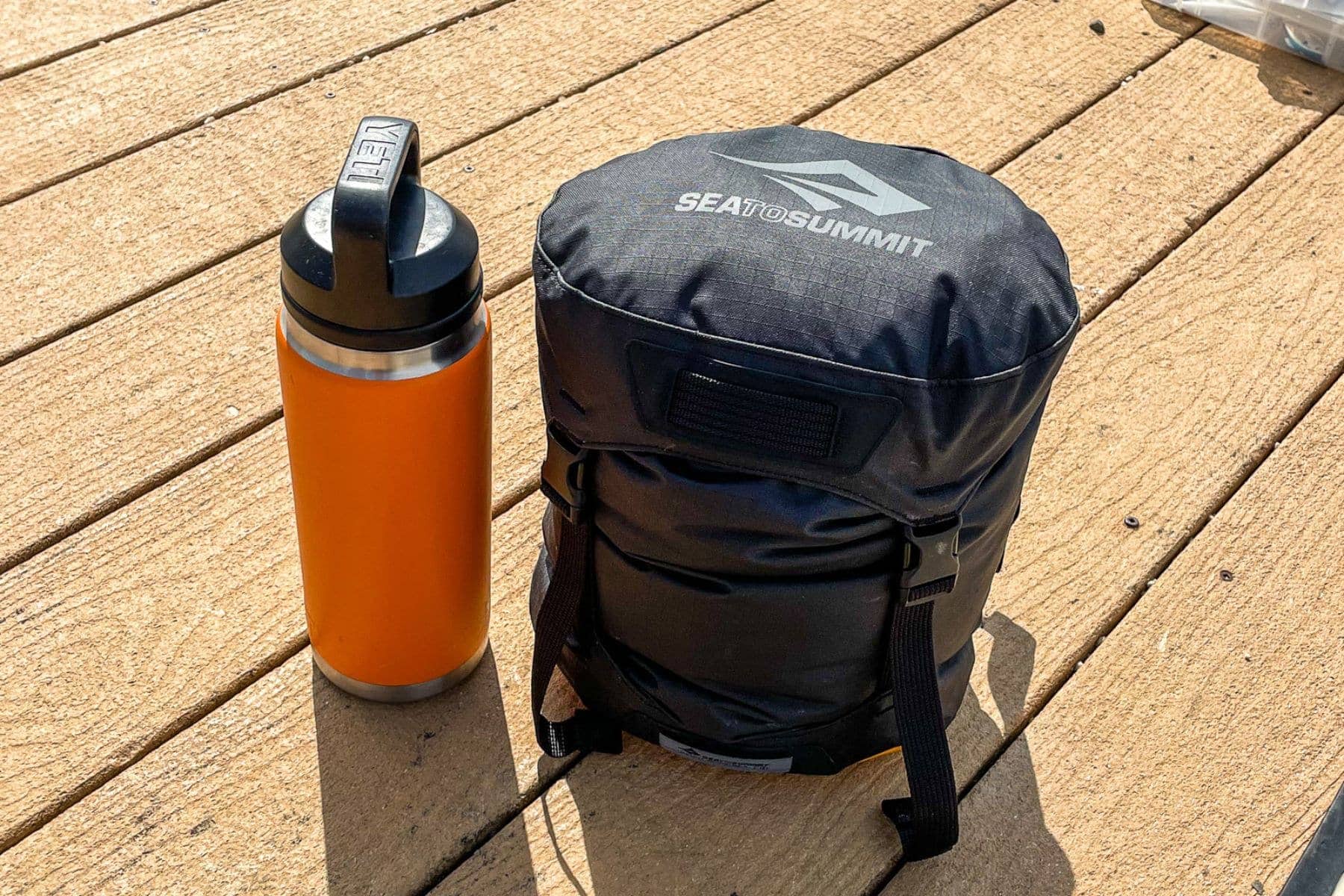 Sea to Summit EVAC Compression HD dry bag standing on a wooden dock beside an orange insulated bottle