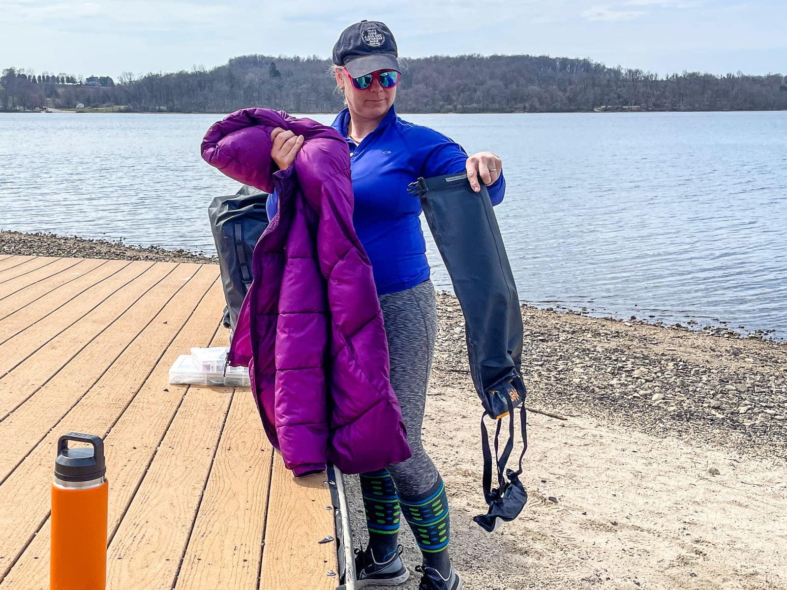 DIVEIN tester on a dock holding a bulky purple down jacket next to the empty Sea to Summit dry bag