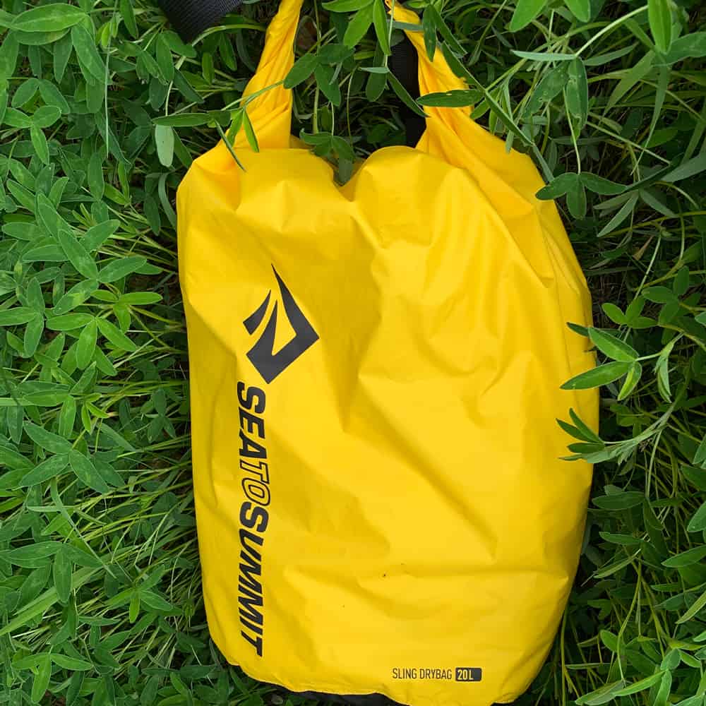 Yellow Sea to Summit Sling Lightweight 20L dry bag laid on grass showing its roll top and logo