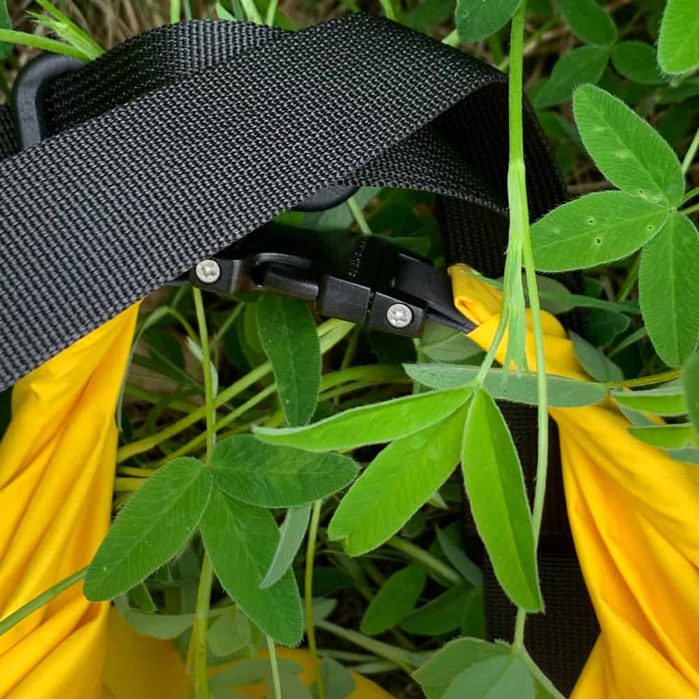 Close-up of the Sling Lightweight's black webbing strap and plastic slider buckle above the yellow bag