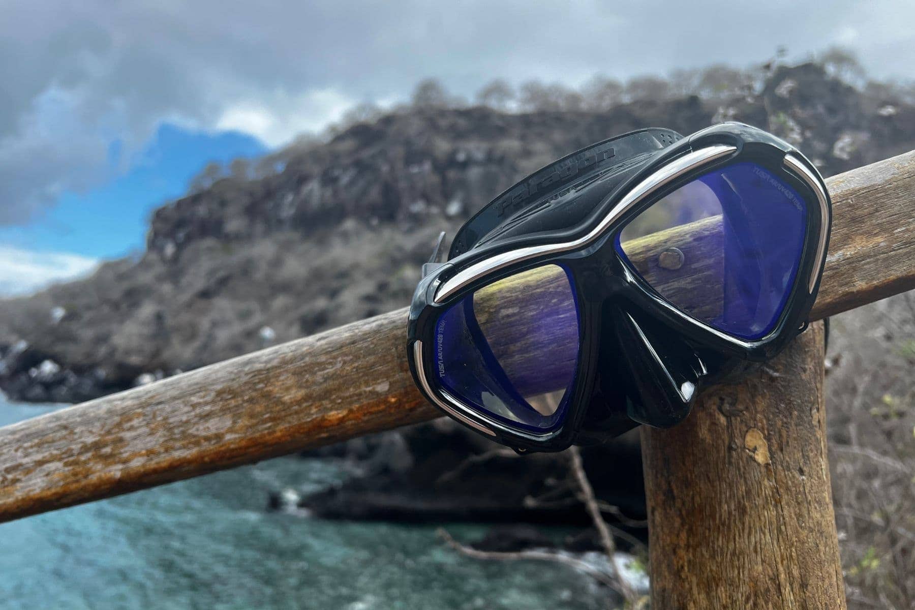 TUSA Paragon mask balanced on a wooden railing above a rocky coastline and turquoise water