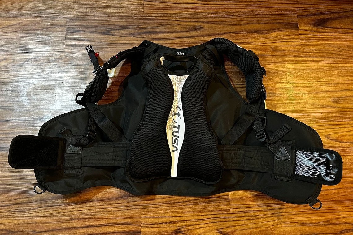 TUSA Tina BCD laid flat on a wooden floor showing its padded back panel and shoulder straps