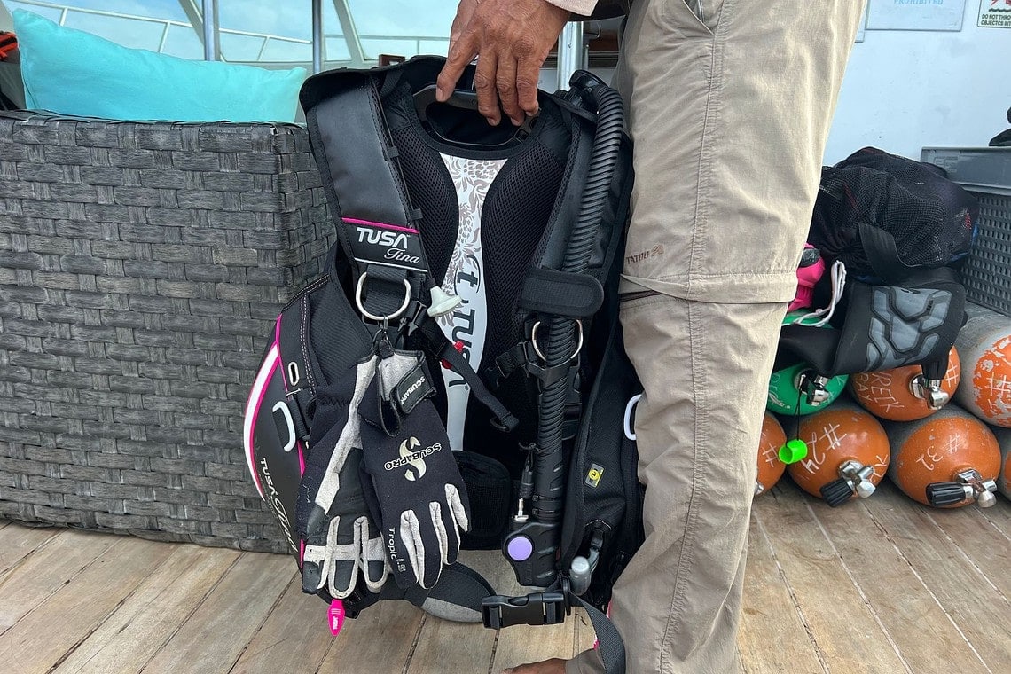 Our tester carrying the TUSA Tina BCD by its handle with dive gloves clipped on and tanks behind