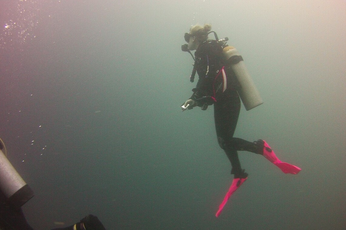DIVEIN tester hovering in midwater wearing the TUSA Tina BCD with pink fins and a single tank