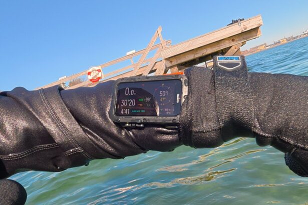 DIVEIN tester checking the Suunto Nautic at the surface with drysuit gloves beside a wooden pier