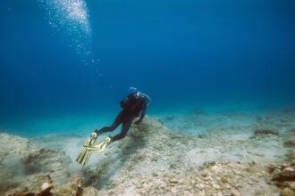 Scuba diver gliding over a sandy seabed with sunlight and bubbles rising overhead