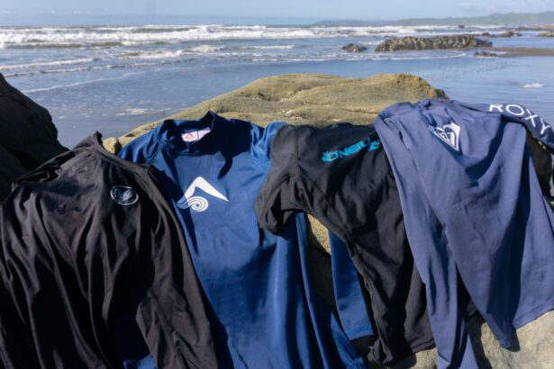 Four rash guards from different brands laid over a rock on the beach with surf breaking behind