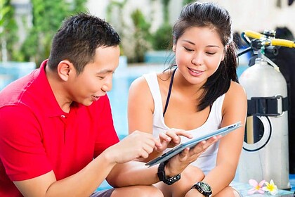 Dive instructor reviewing a tablet with a student beside scuba tanks poolside