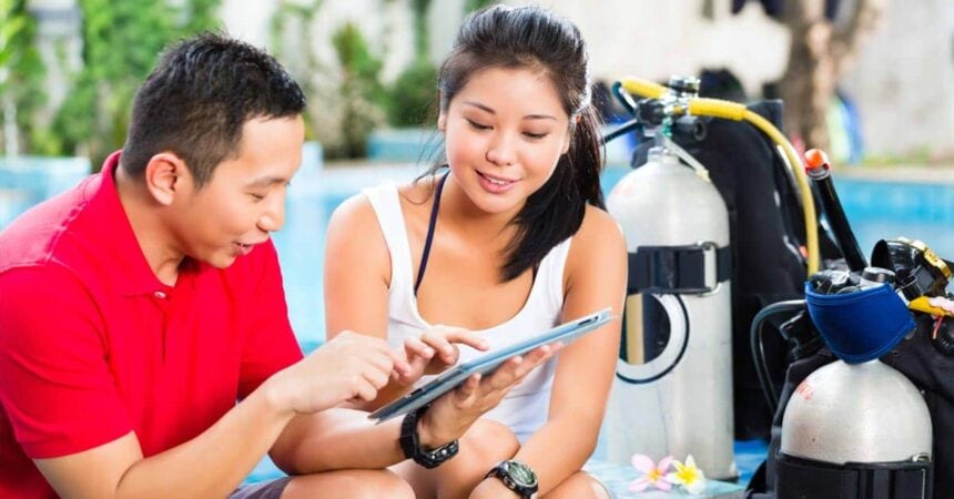 Dive instructor reviewing a tablet with a student beside scuba tanks poolside