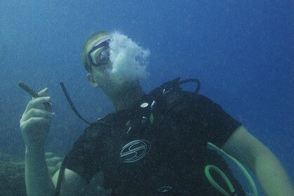 Diver exhales a large bubble ring like smoke while holding a fake cigarette underwater
