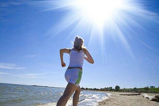 Woman jogging along a beach shoreline with the sun flaring overhead