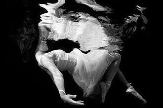 Black and white underwater portrait of a woman in a flowing white dress with hair drifting in water