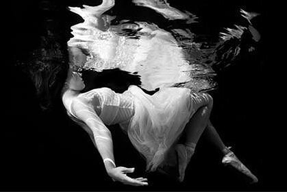 Black and white underwater portrait of a woman in a flowing white dress with hair drifting in water
