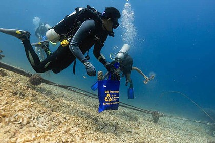 Diver collecting plastic waste in a mesh bag marked Say No to Plastic during a reef cleanup dive