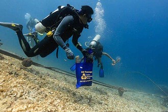Two divers pulling a net full of collected trash and debris off a rocky seafloor