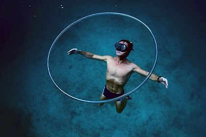 A freediver with arms outstretched floats inside a large hoop in deep blue water