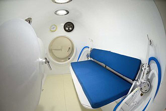 Interior of a hyperbaric recompression chamber with a blue padded bench and pressure gauges