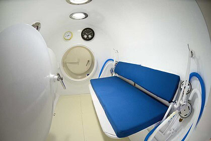 Interior of a hyperbaric recompression chamber with a blue padded bench and pressure gauges