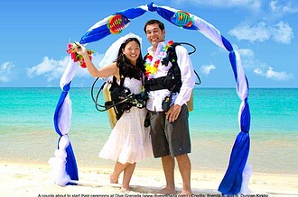 Bride and groom in scuba gear stand under a decorative arch on the beach before their Dive Grenada underwater wedding