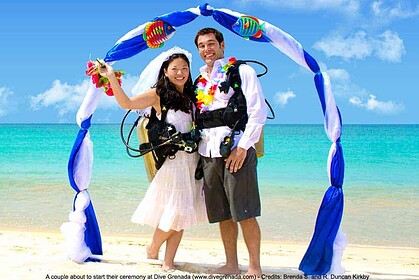 Bride and groom in scuba gear stand under a decorative arch on the beach before their Dive Grenada underwater wedding