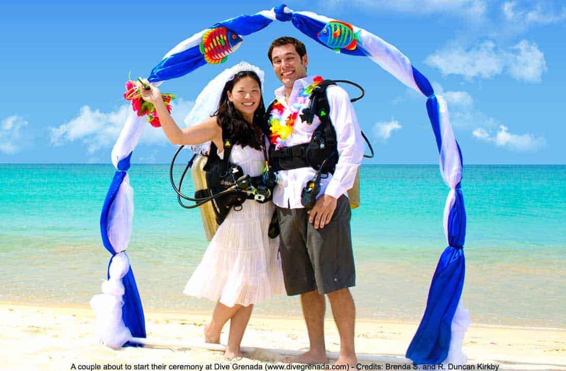 Bride and groom in scuba gear stand under a decorative arch on the beach before their Dive Grenada underwater wedding
