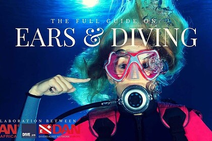 A diver in a pink mask pointing to her ear while surrounded by bubbles, on a guide to ears and diving