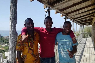 Apprentice divers Fernando and Carlos join a colleague for a photo on a wooden veranda overlooking the ocean in Mozambique