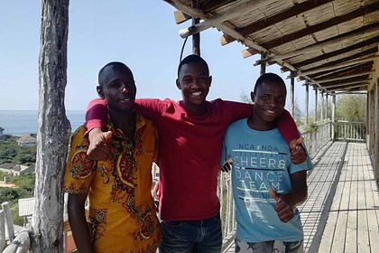 Apprentice divers Fernando and Carlos join a colleague for a photo on a wooden veranda overlooking the ocean in Mozambique